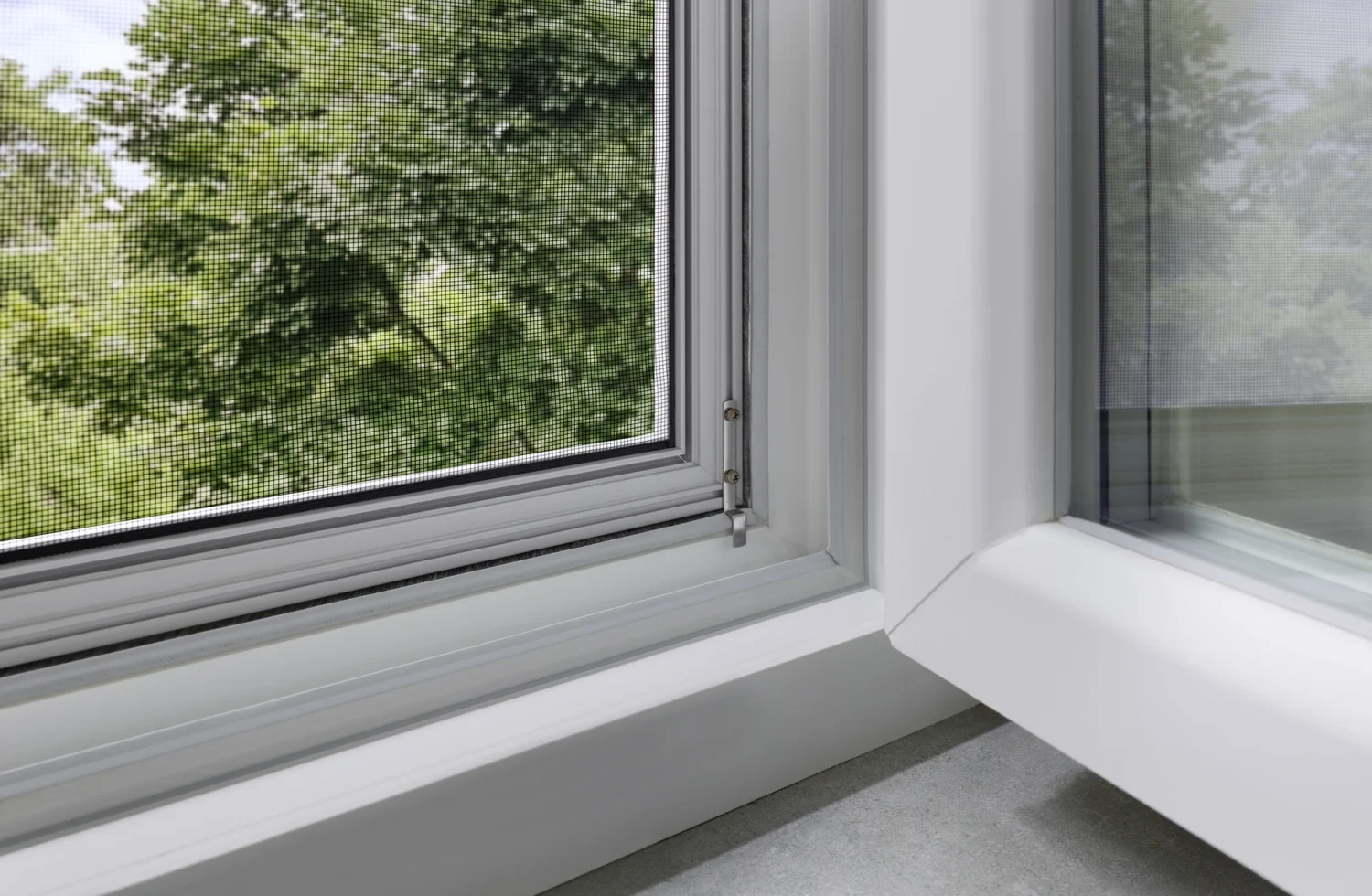 Nahaufnahme eines Fensters mit Fliegengitter und Blick auf grüne Bäume